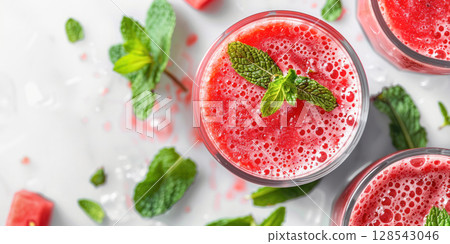 Refreshing watermelon smoothie in clear glasses garnished with mint leaves, surrounded by fresh watermelon pieces and green mint, perfect for summer enjoyment 128543046