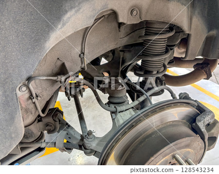 An intricate view of a vehicle's suspension system show various component like shock absorber and brake system in an auto repair facility during daylight hour. An intricate view of a vehicle's suspension system show various component like shock absorber and brake system in an auto repair facility during daylight hour. 128543234