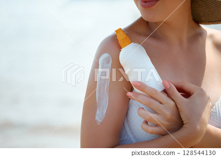 Woman Applying Sunscreen at Beach to Protect Skin From Sunlight 128544130