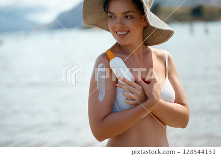 Smiling Woman Applying Sunscreen at Beach on a Sunny Summer Day 128544131