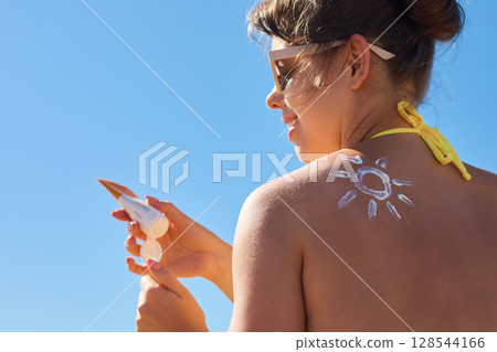Beauty Woman applying sunscreen  on tanned shoulder. Skincare. Body Sun protection suncream. Portrair of female applying moisturizing sunscreen lotion on back 128544166