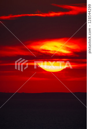 Red sunset over the sea horizon with dark silhouette of distant hills. 128544299