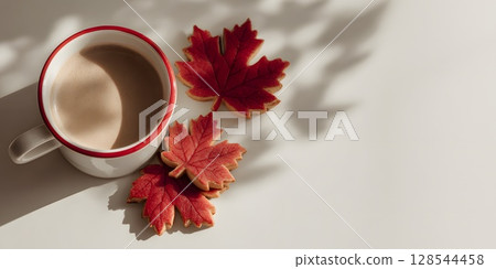 A cup of coffee with a red rim sits beside maple leaf-shaped cookies and real maple leaves. The scene is set for Canada Day celebrations with empty space for text. 128544458