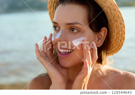 Suntan lotion woman applying sunscreen solar cream. Beautiful happy cute woman applying suntan cream to her nose Suntan lotion woman applying sunscreen solar cream. Beautiful happy cute woman applying suntan cream to her nose 128544643