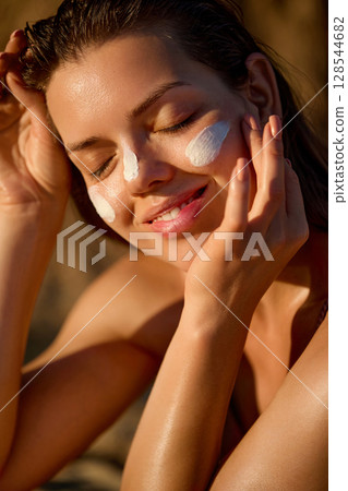 Beauty woman with suntan spf and skincare cosmetics model face portrait, woman with moisturising cream, sunscreen product or sun tan lotion on her cheek, luxury facial and skin care. 128544682