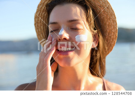 Beautiful young woman with sun cream on face. Girl applying sunscreen lotion on skin.Skin care. Sun protection. Suntan 128544708