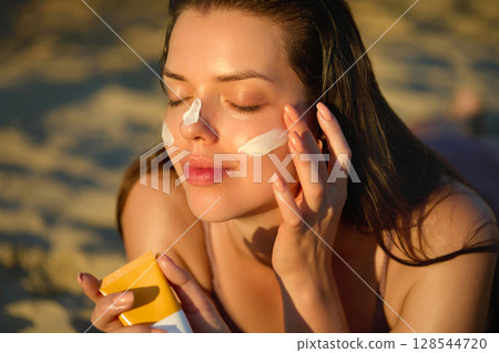Skin care. Sun protection. Woman Applies Sunscreen on Face. Woman With Suntan Lotion On Beach. Portrait of Female With Sun Cream on Shoulder. Girl Holding Moisturizing Sunblock. Skin care. Sun protection. Woman Applies Sunscreen on Face. Woman With Suntan Lotion On Beach. Portrait of Female With Sun Cream on Shoulder. Girl Holding Moisturizing Sunblock. 128544720