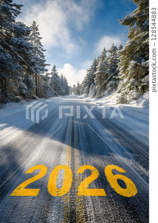 A snowy road leads into the distance, marked with the year 2026 in bright yellow. Pine trees line the sides under a clear blue sky. 128544883