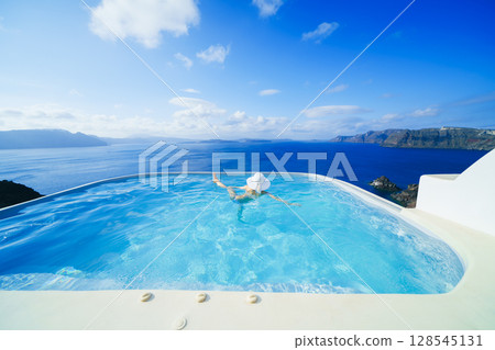 一名女子在希臘聖托里尼島的游泳池裡游泳 128545131