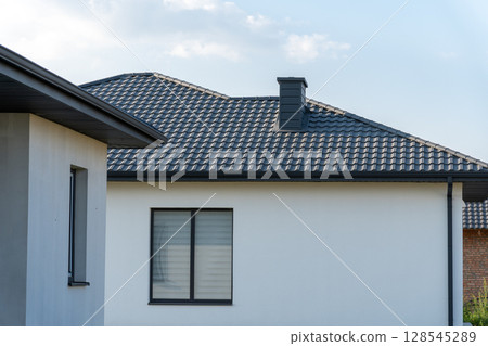 A contemporary house features a well-defined roof, a dark chimney, and large windows under a clear sky, emphasizing its modern design 128545289