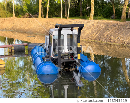 A specialized machine designed for aquatic maintenance operates on a tranquil river, clearing vegetation as the day ends A specialized machine designed for aquatic maintenance operates on a tranquil river, clearing vegetation as the day ends 128545319