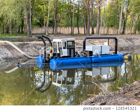 A specialized water management vessel works diligently on a calm pond, managing water levels and ensuring environmental care on a sunny day A specialized water management vessel works diligently on a calm pond, managing water levels and ensuring environmental care on a sunny day 128545321