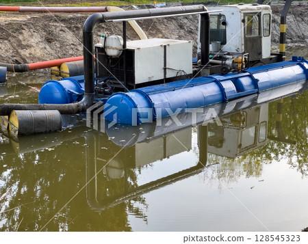 A water cleaning machine works in a tranquil river channel, reflecting nearby greenery. The sunlight highlights its blue and black design A water cleaning machine works in a tranquil river channel, reflecting nearby greenery. The sunlight highlights its blue and black design 128545323