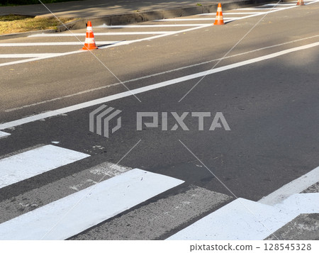 Traffic cones indicate ongoing road work at a pedestrian crossing, enhancing safety in the urban environment under bright sunlight 128545328