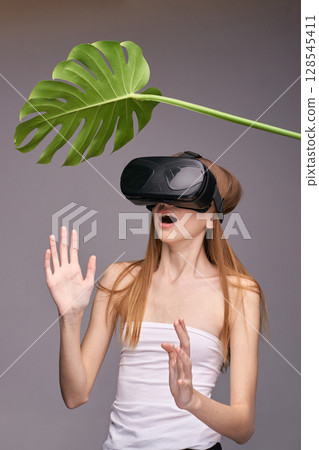 Young caucasian female experiencing virtual reality with headset and monstera Young caucasian female experiencing virtual reality with headset and monstera 128545411