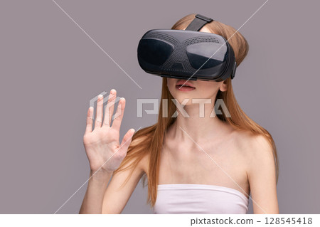 Young caucasian female using vr headset with interactive gesture on gray Young caucasian female using vr headset with interactive gesture on gray 128545418