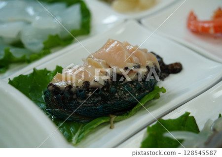 Fresh Abalone Sashimi Slices on White Plate with Green Leaf Garnish 128545587