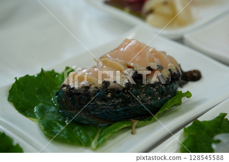Fresh Abalone Sashimi Slices on White Plate with Green Leaf Garnish 128545588