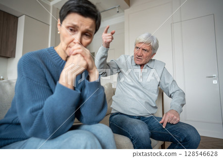 Irate senior man in abusive shouting toward sad wife, family breakdown in emotional control Irate senior man in abusive shouting toward sad wife, family breakdown in emotional control 128546628