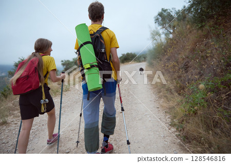 Couple Hiking in Nature with Trekking Sticks and Dog on Mountain Path Couple Hiking in Nature with Trekking Sticks and Dog on Mountain Path 128546816