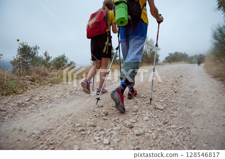 Energetic Young Hikers Exploring a Mountainous Trail with Trekking Poles, Backpacking Gear, and Their Trusty Canine Companion 128546817