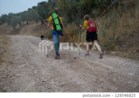 Young Couple Hiking in Nature with Trekking Poles and Dog 128546825