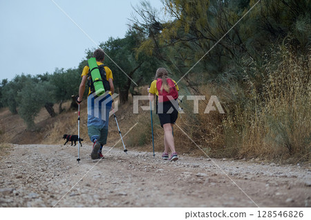 Young Couple Hiking in Nature With Trekking Sticks and Dog Through Scenic Outdoors Young Couple Hiking in Nature With Trekking Sticks and Dog Through Scenic Outdoors 128546826