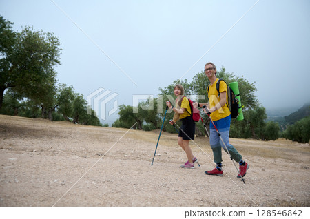 Young Couple Hiking Through Scenic Mountain Trails with Trekking Sticks and Backpacks 128546842