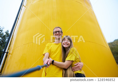 Young Couple Smiling in Front of a Yellow Tower Capturing a Joyful Selfie Young Couple Smiling in Front of a Yellow Tower Capturing a Joyful Selfie 128546852