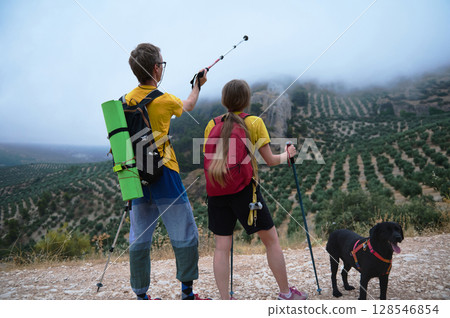 Young Couple Trekking Through Scenic Mountain Landscape With Their Dog 128546854