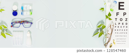 Eye care banner with eyeglasses, containers with contact lenses, vitamins and Snellen table for vision testing on blue background. Concept of eye care, eye treatment and good vision. Copy space 128547460
