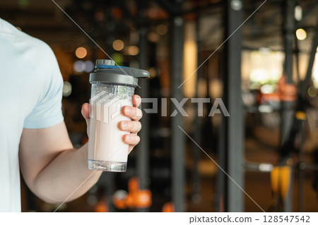 Close up of mans hand with protein shaker at gym. Fitness healthy lifestyle concept. Supplement product, creatine, glutamine for workout. 128547542