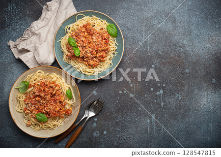 Two plates of spaghetti bolognese with basil on dark background with space for text 128547815