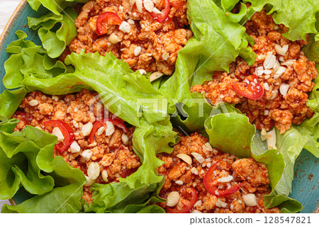 Lettuce wraps filled with minced meat and topped with peanuts and chili pepper flakes on a plate, healthy protein dish 128547821