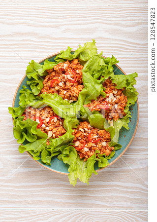 Lettuce wraps filled with minced meat and topped with peanuts and chili pepper flakes on a plate, healthy protein dish 128547823