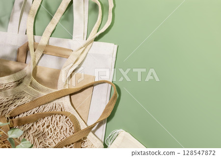 Eco friendly shopping or delivery service. Sustainable still life with textile bags, paper bag and mesh bags on green background. Zero Waste, plastic free, eco packaging concept. Copy space 128547872