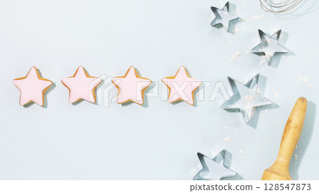 Cooking holiday cookies. Bakery kid flat lay. Ginger cookies in the form of stars, covered with pink glaze, cookie cutters, a dough gurney and a whisk on a blue background. Christmas and New Year Food 128547873