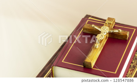 Religion composition with wooden crucifix with closed red Christian bibles on a light gradient background with divine light. Bible and Scripture Study. Religious church holidays. Copy space 128547886