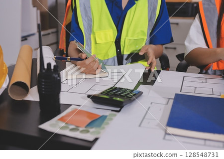 Closeup of team of industrial engineers meeting analyze machinery blueprints consult project on table in manufacturing factory. Working in manufacturing plant or production plant. 128548731