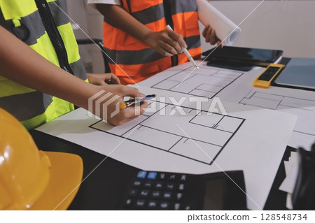 Closeup of team of industrial engineers meeting analyze machinery blueprints consult project on table in manufacturing factory. Working in manufacturing plant or production plant. 128548734