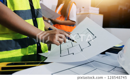 Closeup of team of industrial engineers meeting analyze machinery blueprints consult project on table in manufacturing factory. Working in manufacturing plant or production plant. 128548745