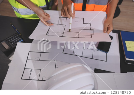 Closeup of team of industrial engineers meeting analyze machinery blueprints consult project on table in manufacturing factory. Working in manufacturing plant or production plant. 128548750