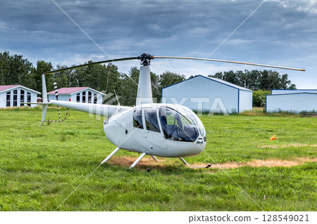 Private small white helicopter on green field near cottages Private small white helicopter on green field near cottages 128549021