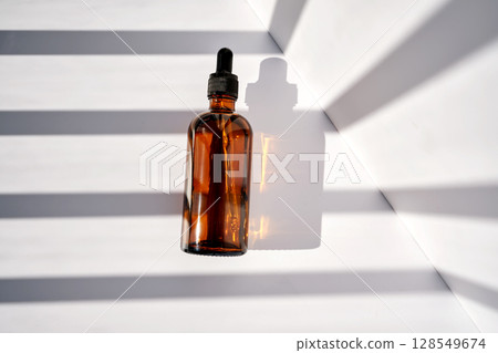A bottle of serum made of brown glass on a white background with stripes of light. A bottle of serum made of brown glass on a white background with stripes of light. 128549674