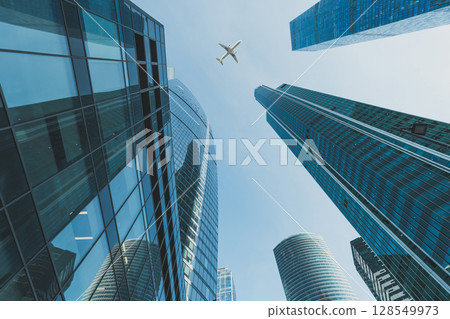 Modern glass skyscrapers and passenger airliner flying over them 128549973
