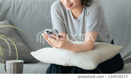 Smiling woman sitting on sofa and using smartphone 128550537
