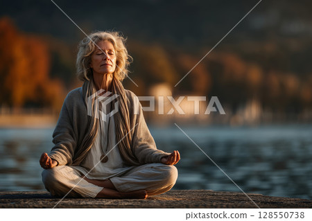 Senior woman finds tranquility meditating by a serene lake in morning light Senior woman finds tranquility meditating by a serene lake in morning light 128550738