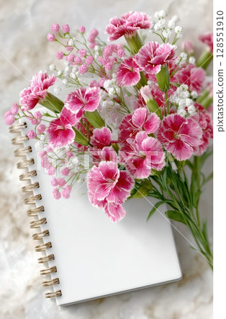 Elegant notebook mockup with floral decor on marble, top view for product display, branding, or social media visuals with pastel aesthetic. 128551910