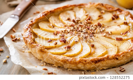Rustic pear and goat cheese pie with golden crust, layered pear slices, crumbled nuts, and cozy artisan presentation on parchment paper 128552275