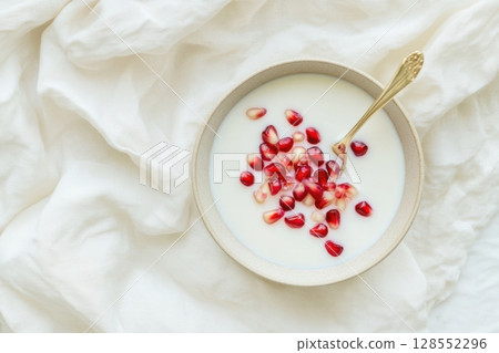Minimalist bowl of coconut milk with muted pomegranate seeds, styled in soft creamy tones on textured linen for a serene modern food concept. 128552296